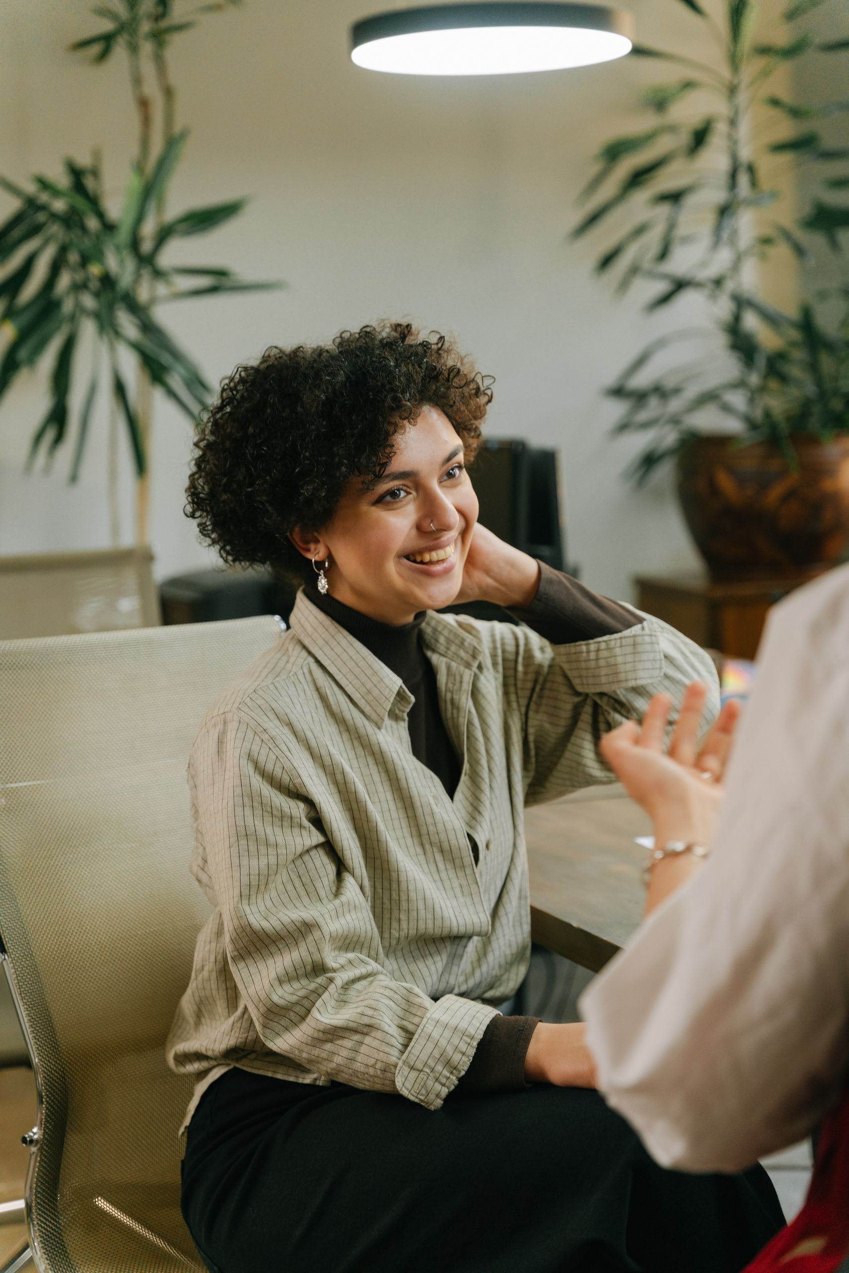 Smiling woman with curly hair having a conversation in an indoor office environment.